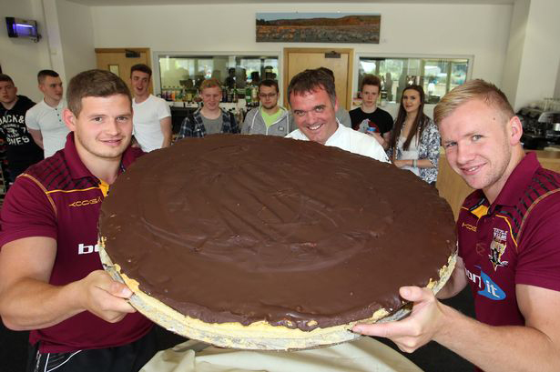Kirklees College Hospitality and Catering Team Leader Gary Schofield offers Huddersfield Giants players Jacob Fairbank and Aaron Murphy a bite